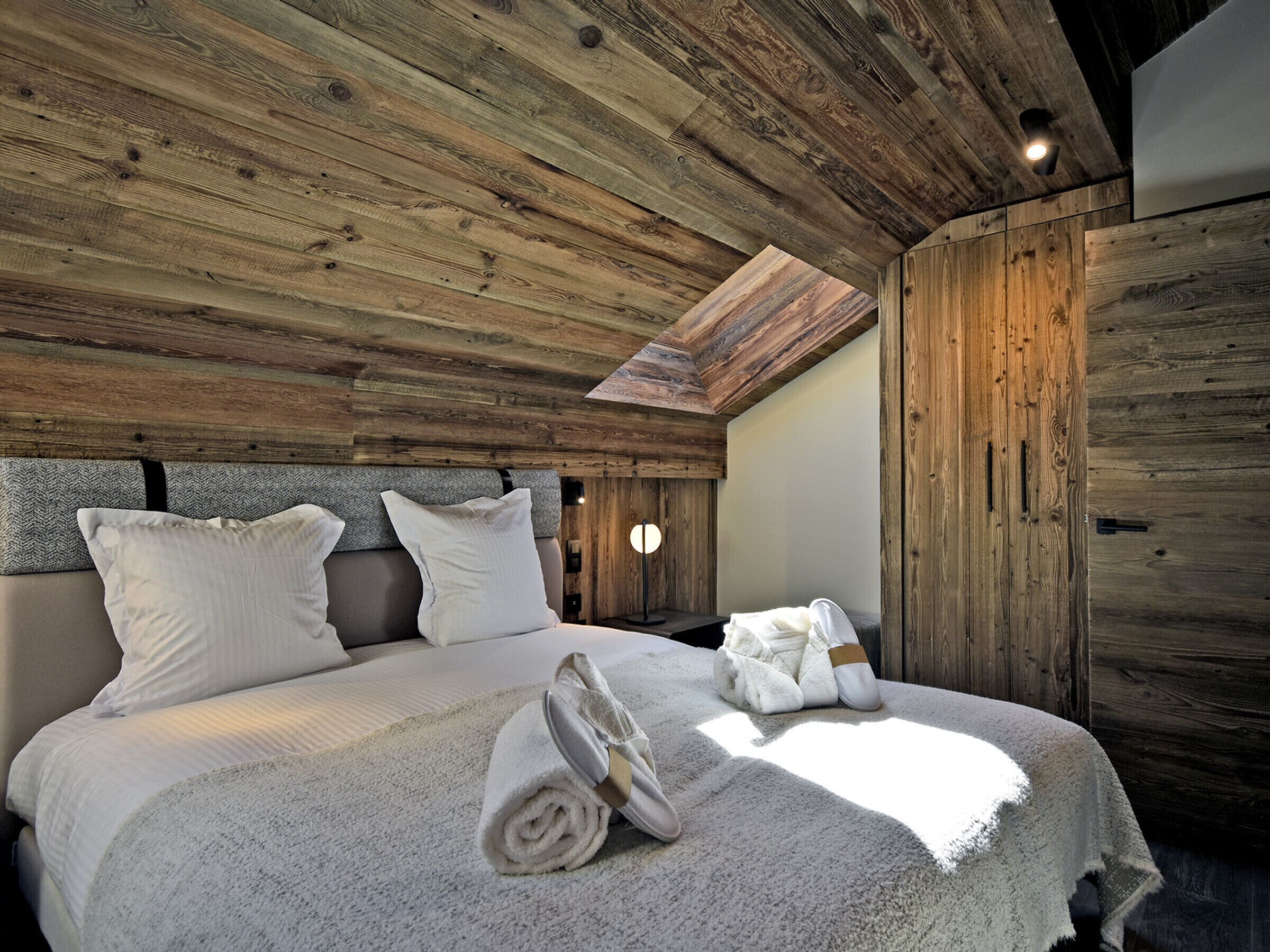 A wooden ceiling with a skylight, a bed with white bedding, and a towel on the bed.