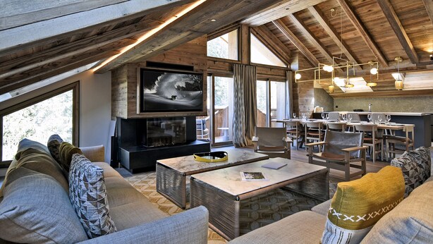 Un intérieur chaleureux et rustique, avec un plafond haut, des poutres en bois, une cheminée, un téléviseur et un coin repas.