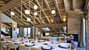 Un espace repas avec une longue table en bois dressée pour un repas, entourée de chaises en bois.