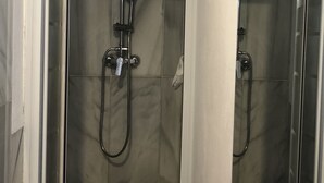 Ein Badezimmer mit einem weißen Waschbecken, einer Duschkabine aus Glas und einem Spiegel, der den Duschbereich reflektiert.