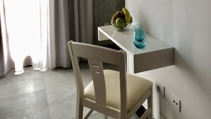 Une chambre moderne avec un téléviseur à écran plat fixé au mur, un bureau blanc sur lequel se trouve un bol de fruits et un verre, ainsi qu’une chaise.