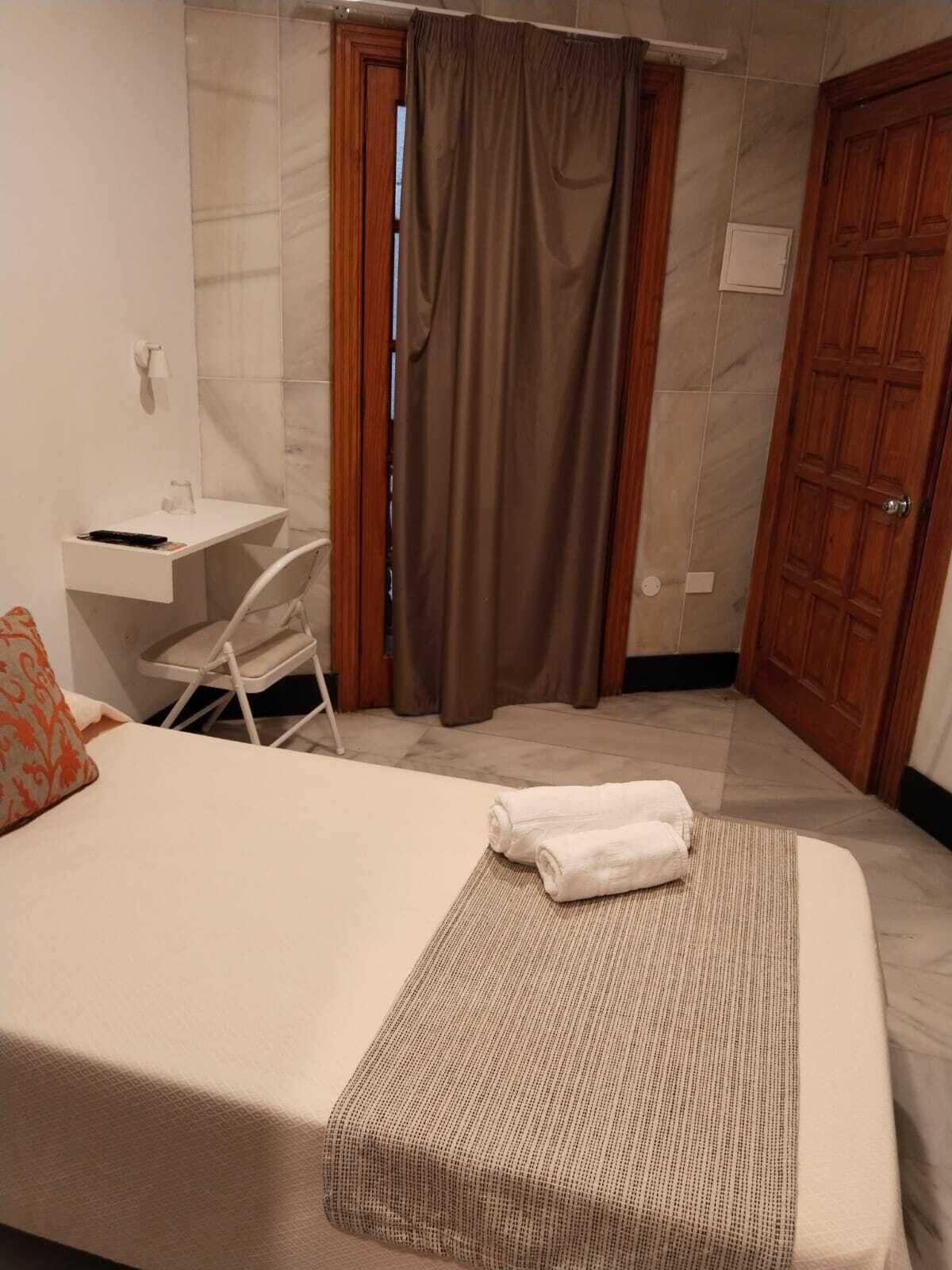 Habitación de hotel con cama, escritorio, silla y baño con cortina de ducha, además de una puerta de madera.