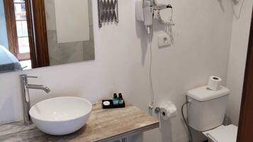 Un baño con lavamanos blanco, espejo, secador de pelo y retrete.