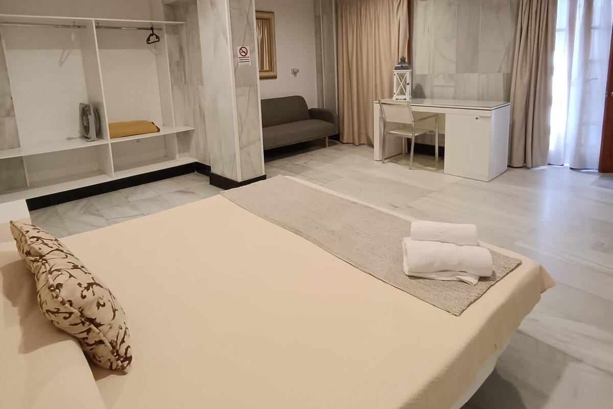 Une chambre d’hôtel avec un lit, un bureau, une armoire et une fenêtre avec des rideaux.