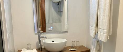 Un baño con un lavamanos blanco, un espejo y un perchero para toallas.