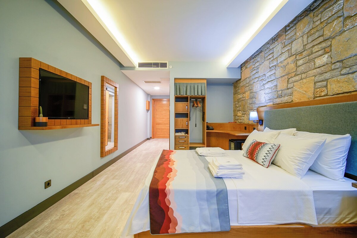 Una habitación de hotel con cama, televisor, armario y pared de piedra.