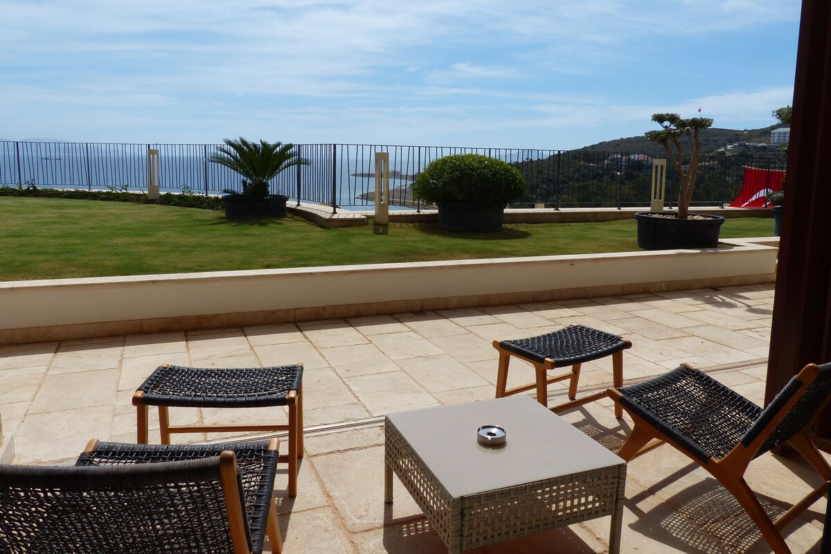 A terrace with wicker furniture, a small table, and a view of the sea.