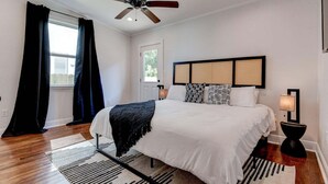 A bedroom with a bed, a ceiling fan, a window with curtains, a nightstand with a lamp, and a headboard with a woven panel. - Updated 3BR Mid-City home with private pool. Steps to streetcar, near FQ & parade route. (New Orleans)