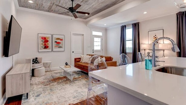 A modern kitchen with a central island, a dining area with a sofa, and a living room with a TV and artwork. - Updated 3BR Mid-City home with private pool. Steps to streetcar, near FQ & parade route. (New Orleans)