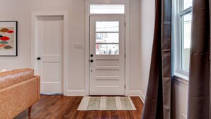 A hallway with a white door, a brown leather sofa, and a window with curtains. - Updated 3BR Mid-City home with private pool. Steps to streetcar, near FQ & parade route. (New Orleans)