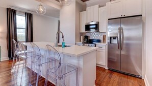 A modern kitchen with a central island, stainless steel appliances, and clear plastic chairs. - Updated 3BR Mid-City home with private pool. Steps to streetcar, near FQ & parade route. (New Orleans)