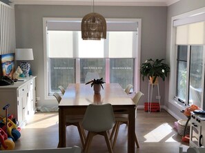 Enjoy meals in this spacious dining area with a large table and six chairs, surrounded by natural light and a potted plant.