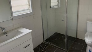 Une salle de bain avec une douche à parois de verre, un lavabo blanc avec un miroir au-dessus et des toilettes.