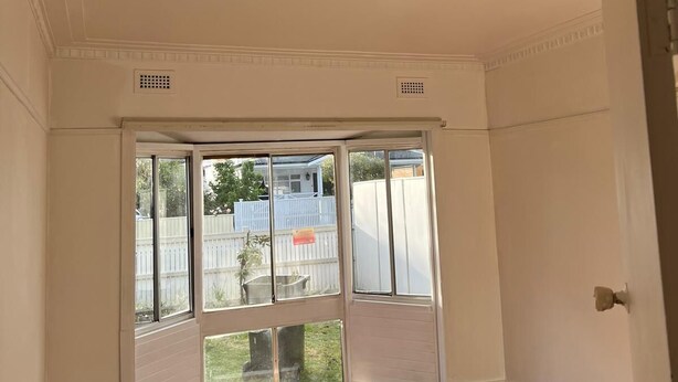 Une pièce dotée d’une grande porte-fenêtre coulissante donnant sur un jardin, de murs blancs et d’un plancher en bois.