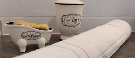 A white towel rolled up on a wooden surface, a small white ceramic container with a lid, and a smaller ceramic container with a lid.
