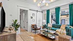 A modern living room with a green sofa, a coffee table, and a TV. There is a plant and a lamp on a side table. - Field of Dreams (Atlanta)