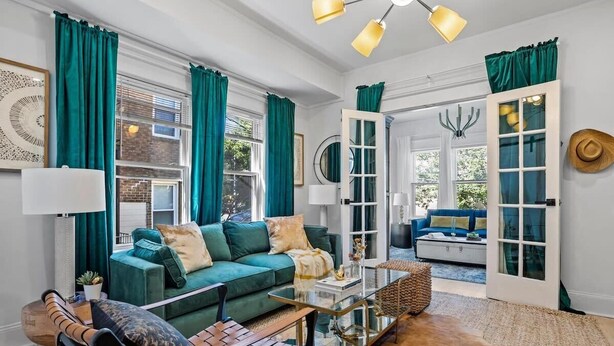 A modern living room with a green sofa, a leather chair, a glass coffee table, and a large window with teal curtains. - Field of Dreams (Atlanta)