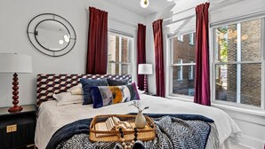A bedroom with a large bed, a round mirror, and a window with curtains. - Field of Dreams (Atlanta)