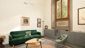 A room with a green sofa, a round table, a green armchair, a large window, and framed artwork on the walls. - Fantastic 3 bedroom apartment in the heart of Florence (Firenze)
