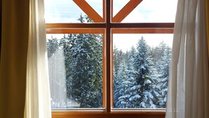 A window with a wooden frame and white curtains, offering a view of snow-covered trees. - Pohorje Village Wellbeing Resort – Family Apartments Bolfenk (Maribor)