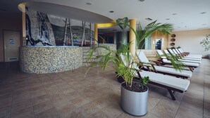 A lobby with a mosaic wall, a reception desk, and sun loungers. - Pohorje Village Wellbeing Resort – Family Apartments Bolfenk (Maribor)