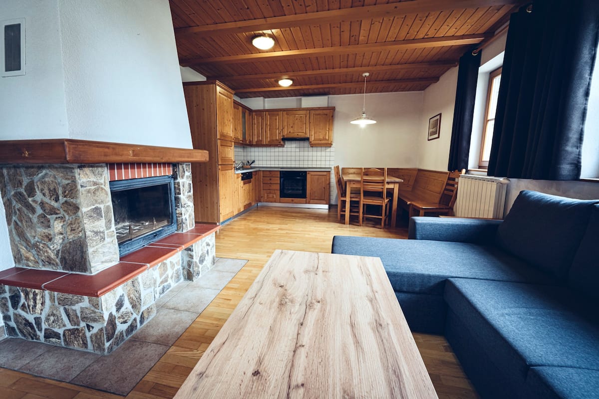 Ett mysigt vardagsrum med en steneldstad, träpanel i taket och en blå soffa.
