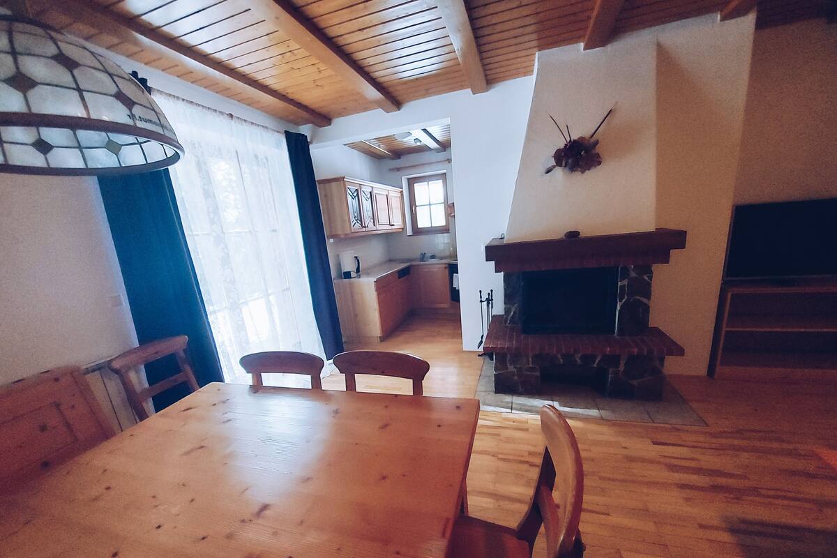 En matplats med ett träbord och stolar, ett kök i bakgrunden och en öppen spis.
