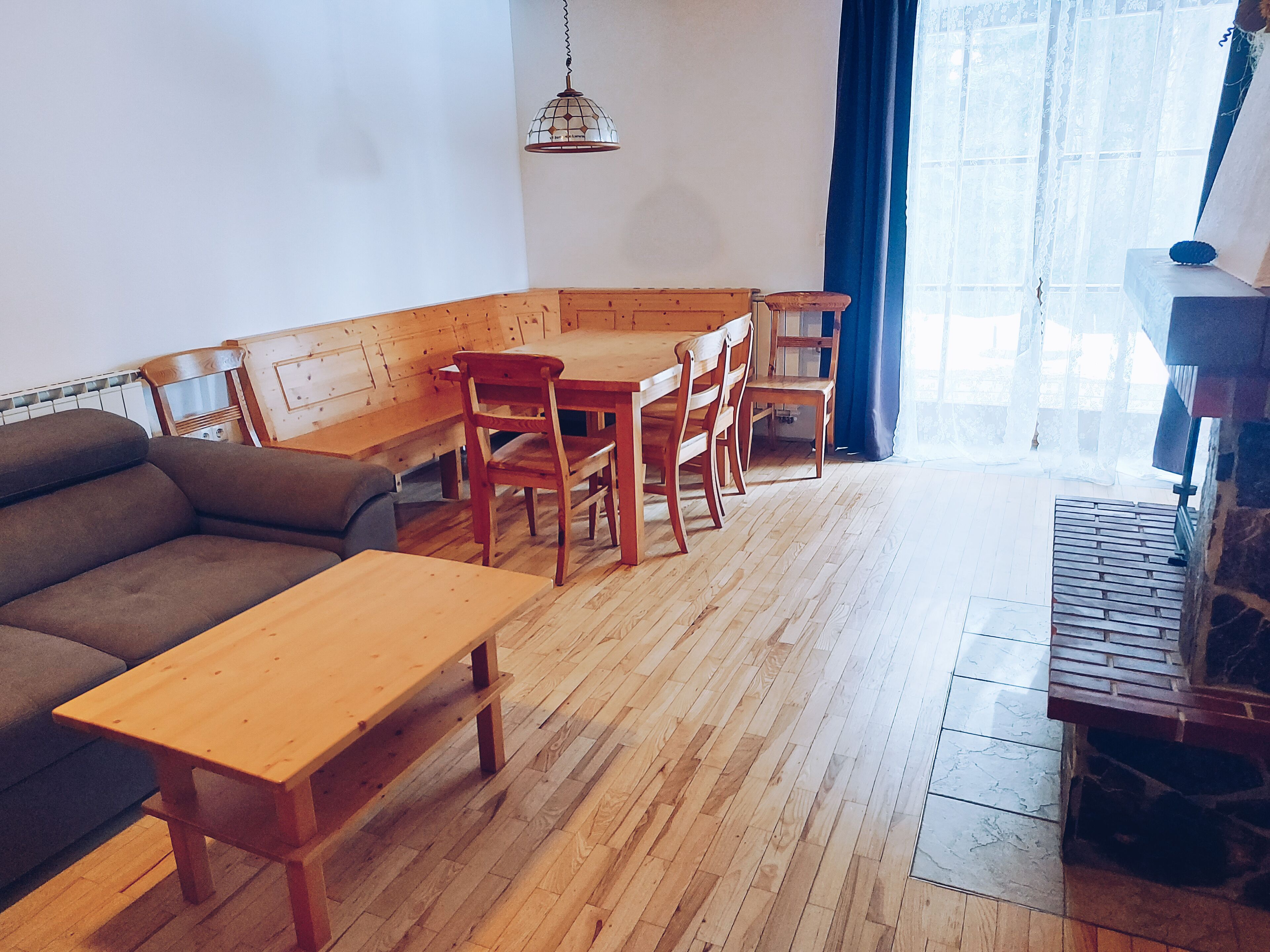 A cozy living room with a wooden bench, a sofa, and a dining table with chairs.