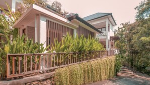 Una casa moderna de dos pisos con balcón, rodeada de abundante vegetación y un jardín cuidado.