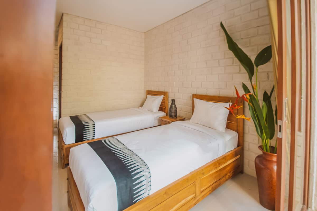 A room with two wooden beds, white bedding, a brick wall, and a potted plant.