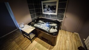 Une salle de bain avec une baignoire noire, une petite table sur laquelle se trouvent une bouteille et des verres, et un tableau encadré accroché au mur.