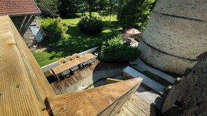 Une terrasse en bois avec une table et des chaises, donnant sur un jardin agrémenté d’une structure en pierre.