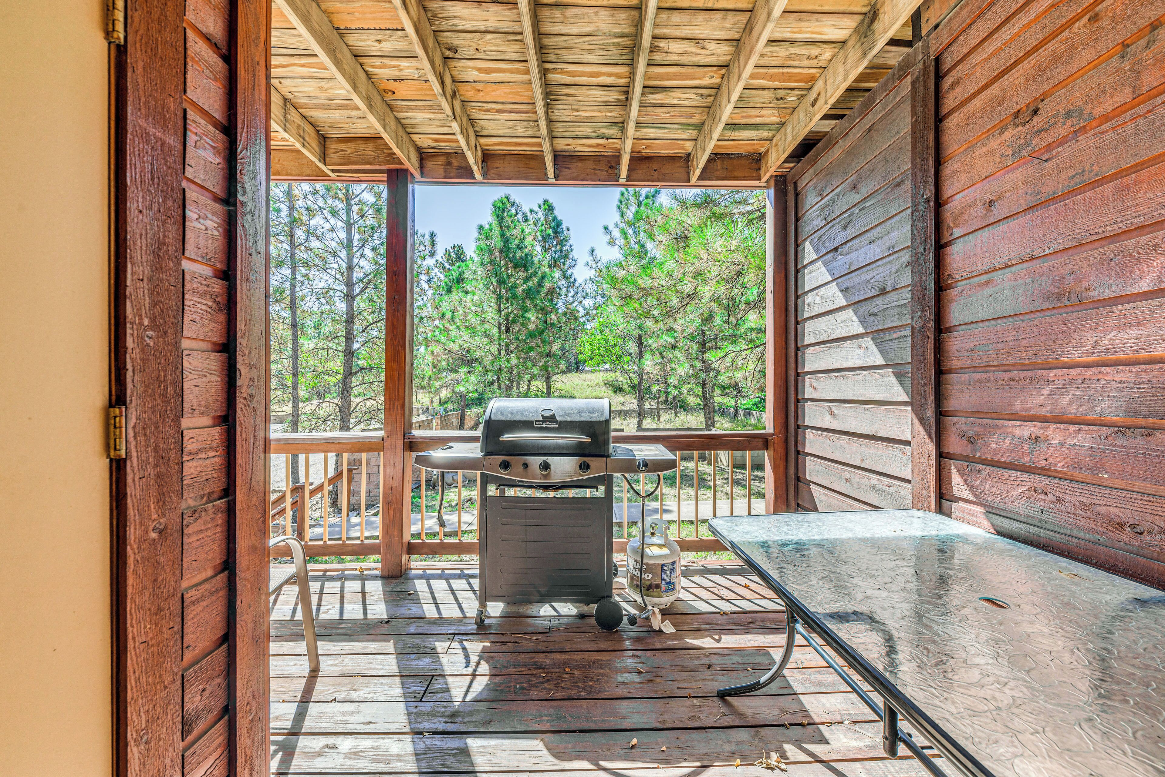 Una terraza de madera con una parrilla y una mesa, con vista a un área boscosa.