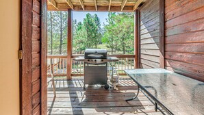 Een houten terras met een barbecue en een tafel, met uitzicht op een bebost gebied.