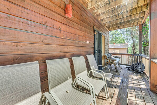 A wooden deck with three wicker chairs and a table, a red lantern, and a view of trees through a door.