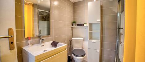 A modern bathroom with a white sink, beige vanity, a toilet, and a glass shower enclosure.