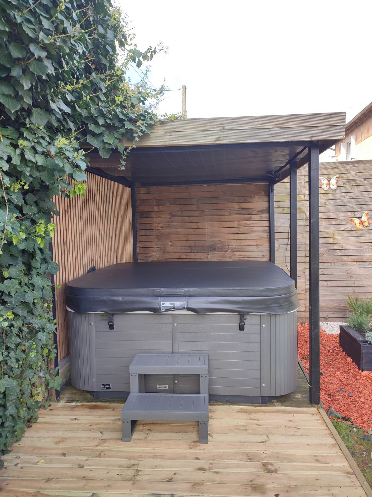 Un bain à remous installé sur une terrasse en bois, entouré d’une clôture en bois et agrémenté de quelques plantes.