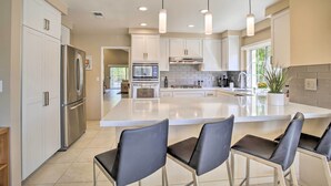 A modern kitchen with white cabinets, stainless steel appliances, and a large island with bar stools. - Desert Retreat - Walk to Indian Wells Tennis (Palm Desert)