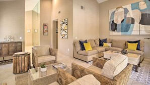 A spacious living room with a large sectional sofa, a coffee table, and a decorative rug. There is a wooden sideboard and a round wooden stool. - Desert Retreat - Walk to Indian Wells Tennis (Palm Desert)