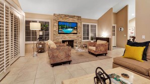 A spacious living room with a stone fireplace, a flat-screen TV mounted above it, and a comfortable seating area with sofas and a coffee table. - Desert Retreat - Walk to Indian Wells Tennis (Palm Desert)