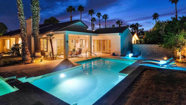 A swimming pool with a modern design, surrounded by palm trees and a well-lit patio area. - Desert Retreat - Walk to Indian Wells Tennis (Palm Desert)