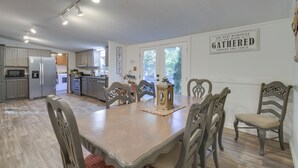 Un'ampia cucina con elettrodomestici moderni, una zona pranzo con sedie e tavolo in legno, e un cartello al muro con la scritta: "I migliori ricordi si creano riuniti attorno alla tavola."