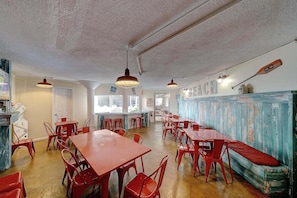 A dining area with red tables and chairs, a wooden bench, and a wall with a 'BEACH' sign. - FREE Golf+Perks!Top of the Gulf Beachfront 703 Spacious Studio w/Great Views! (Panama City Beach)