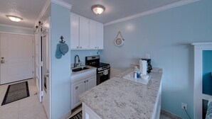 Cocina compacta con gabinetes blancos, encimera de granito, estufa y lavamanos.