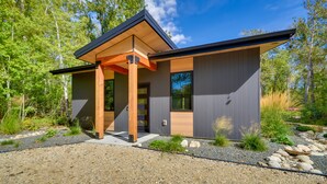 Ein modernes Haus mit einer Holzveranda, großen Fenstern und einer Schotterauffahrt.