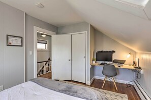 Ein Schlafzimmer mit einem Bett, einem Schreibtisch mit Computer und einem Stuhl. Ein Fenster und eine Tür führen zu einer Treppe.
