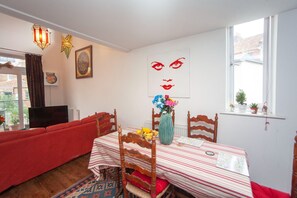 Un coin repas avec une table dressée pour deux personnes, un canapé rouge et un téléviseur en arrière-plan.