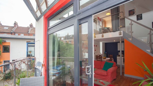 A modern apartment with a glass door leading to a balcony, a red sofa, and a staircase. - Special 3 Bedroom Townhouse With Parking in Bristol (Bristol)