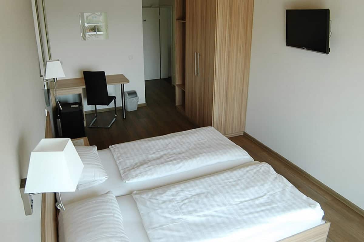 A hotel room with a bed, a desk, a chair, a wardrobe, and a TV.