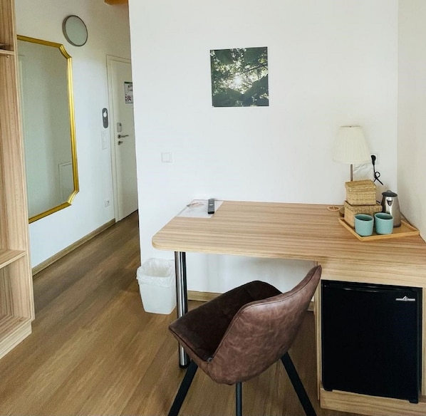 A compact kitchen with a wooden countertop, a small refrigerator, a chair, and a trash bin.